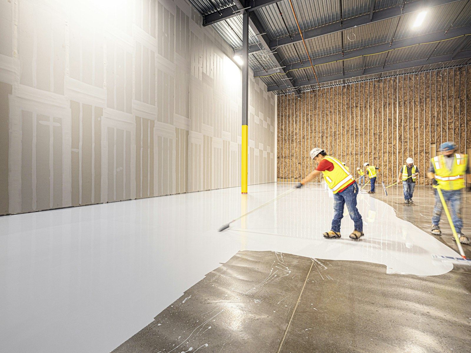 Workers in hi-vis painting a large industrial floor white